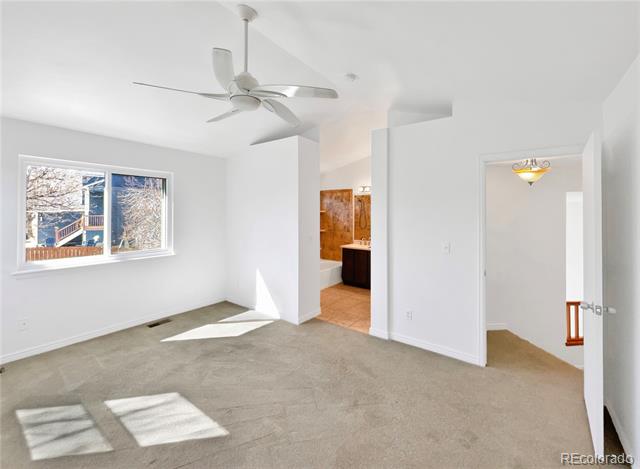 Empty carpeted room with a ceiling fan, wide window, and open doorways.