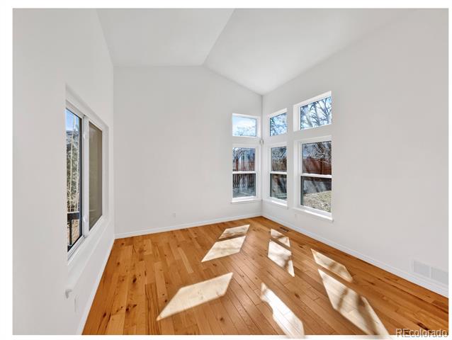 Bright, empty sunroom with hardwood floors, a vaulted ceiling, and tall windows.