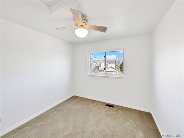 Empty carpeted room with a ceiling fan and a window overlooking neighboring homes.