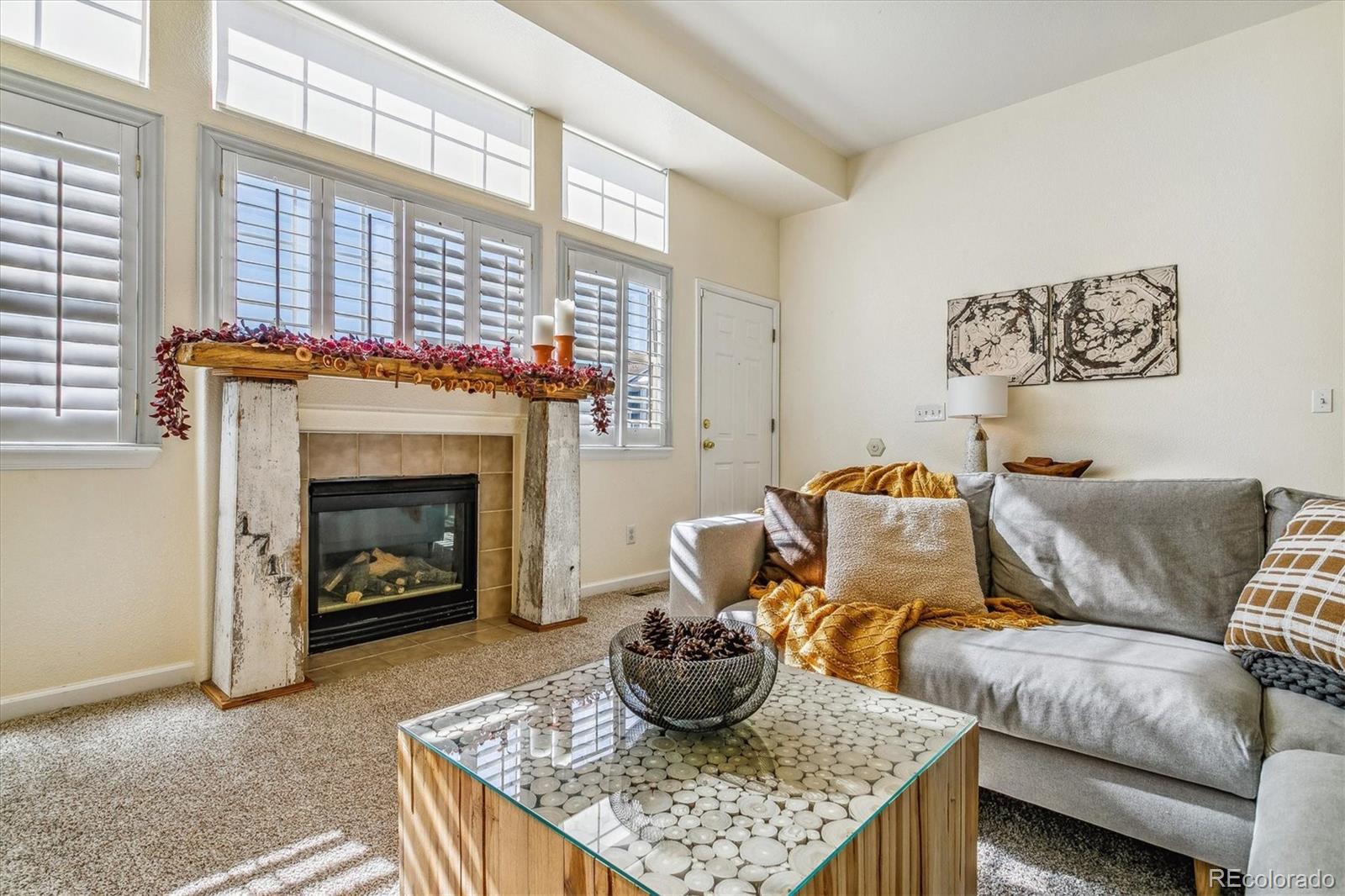 Living room with a tiled fireplace, tall shuttered windows, and a gray sectional sofa.