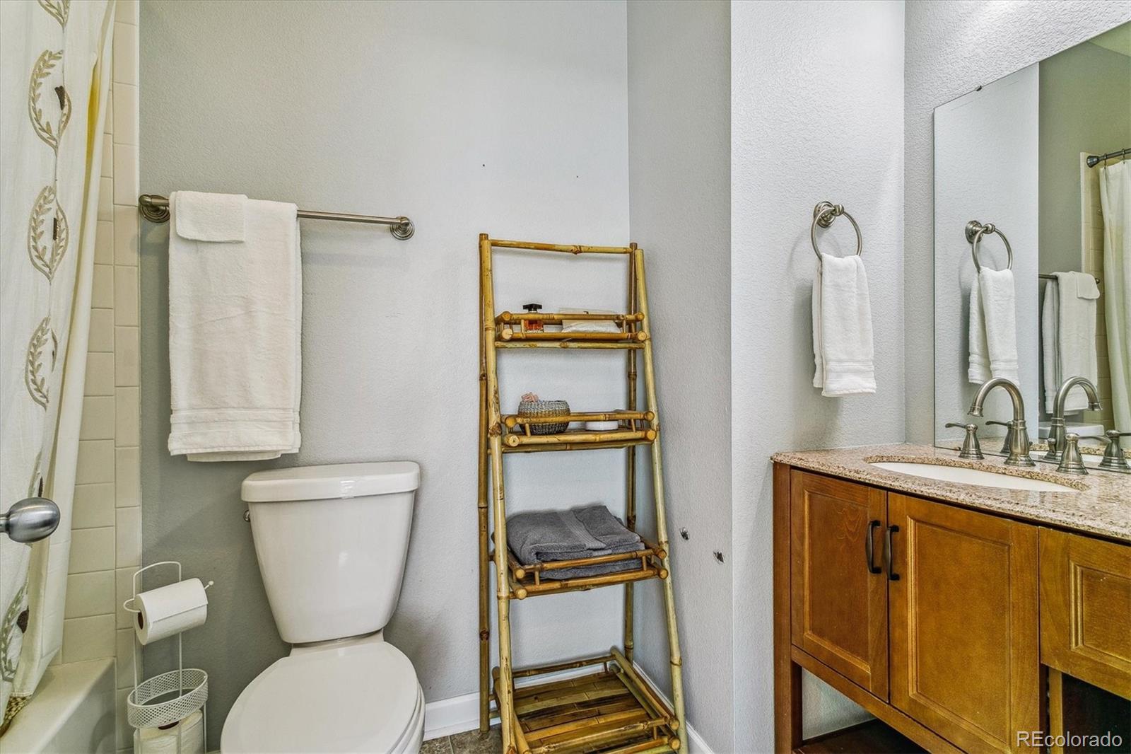 Bathroom with a wooden vanity, large mirror, toilet, and bamboo towel shelf.