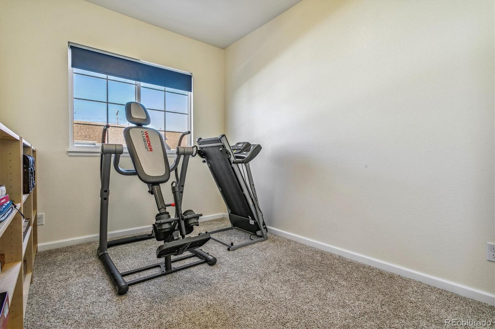 Workout room with an exercise machine, treadmill, and blue-shaded window.