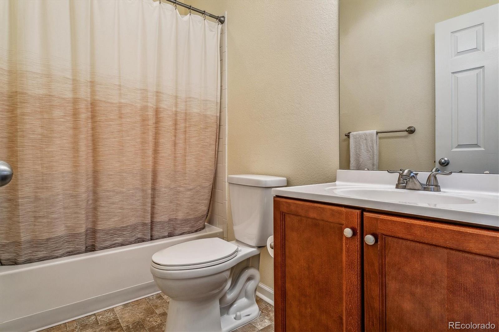 Bathroom with a tub-shower, toilet, and wood vanity topped with a white countertop.