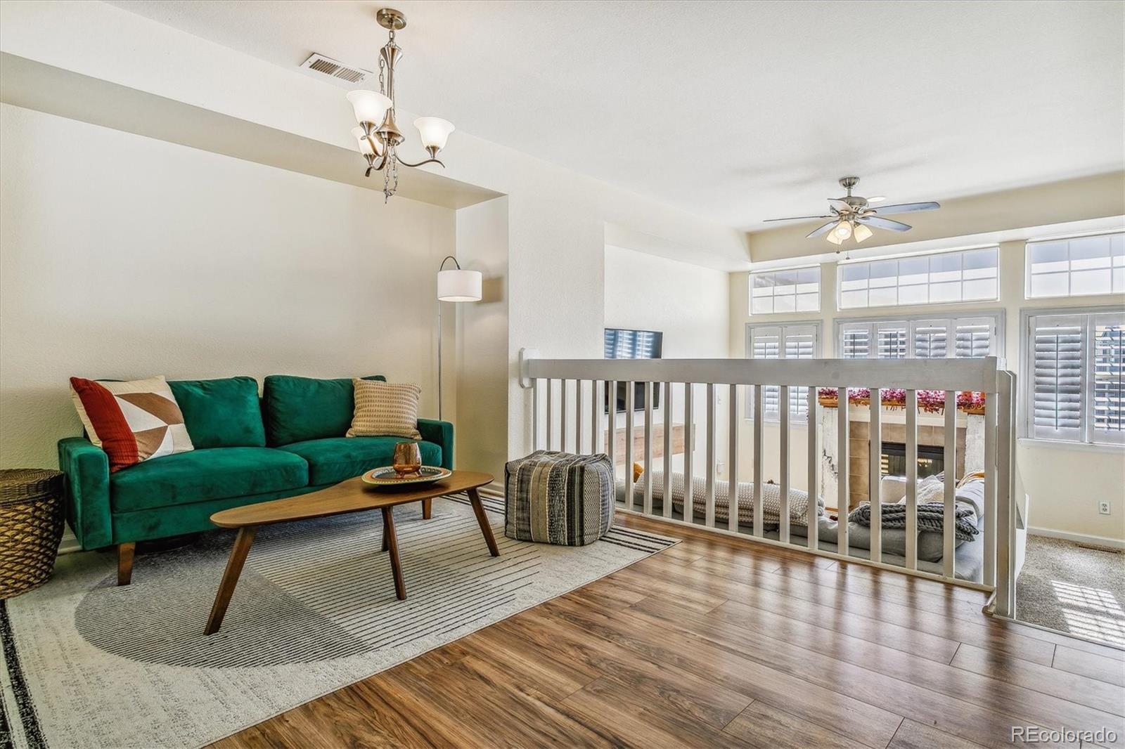 Loft living room with emerald sofa, wood floors, and railing overlooking a lower-level sitting area.
