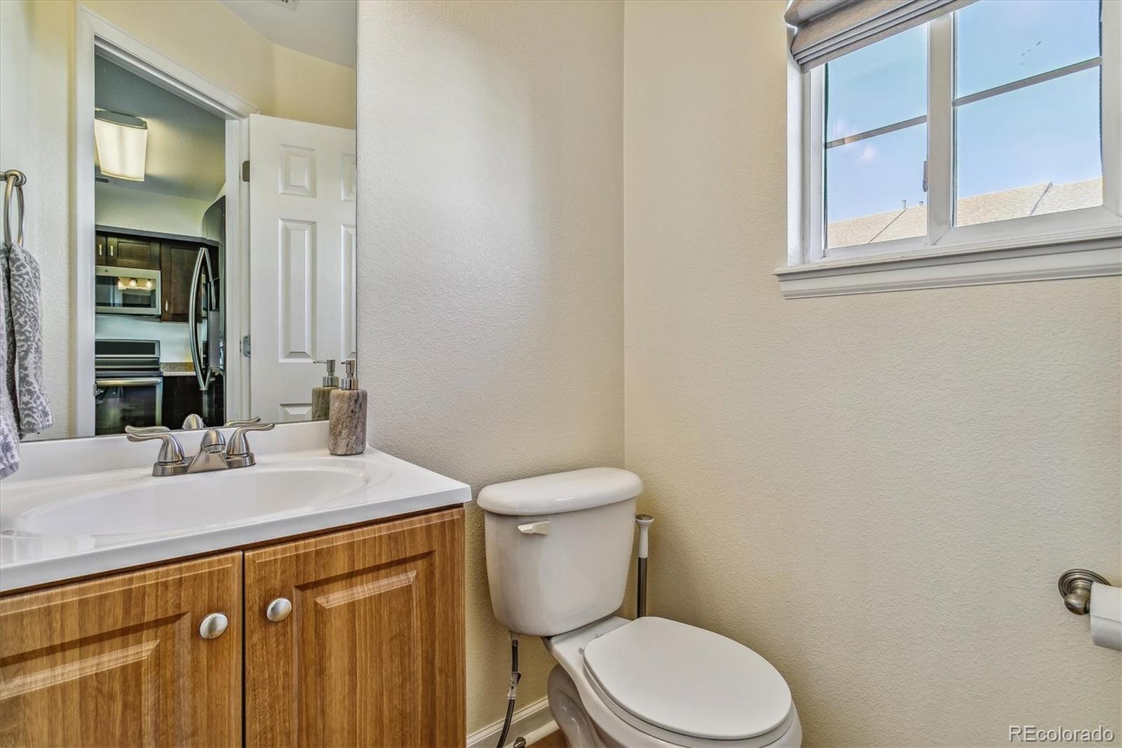 Bathroom with a wood vanity and high window; the mirror reflects the kitchen.