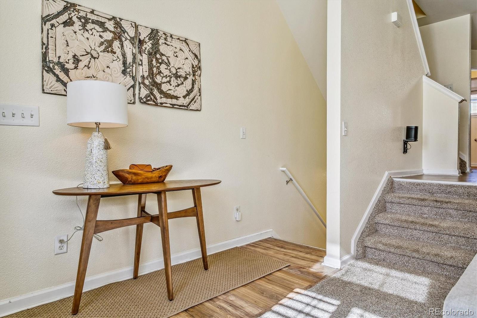 Entryway with a wooden console table and lamp beside a carpeted staircase.