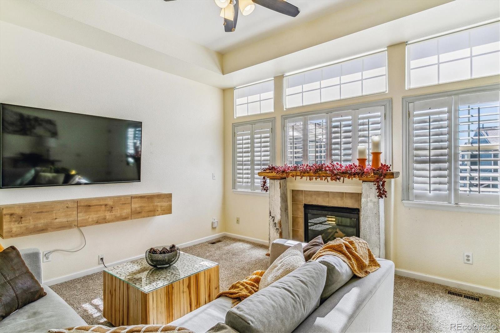Living room with a fireplace, tall shuttered windows, and a wall-mounted television.
