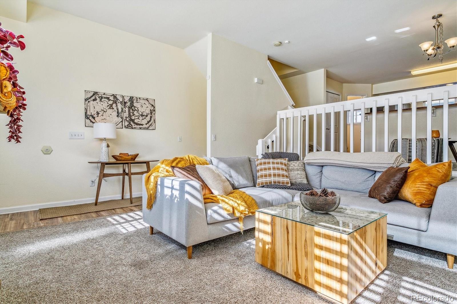 Furnished living room with a gray sectional, wood coffee table, and staircase behind a white railing.