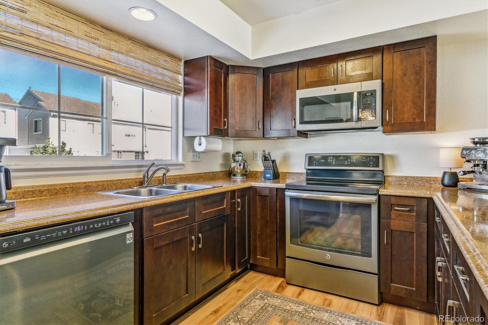 Kitchen with dark wood cabinets, stainless steel appliances, granite counters, and a large window.