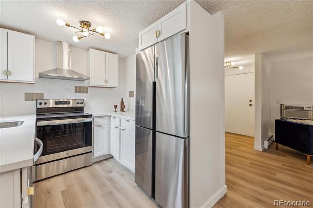 Kitchen with white cabinets and stainless steel appliances, opening to a living area.