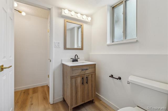 Bathroom with a wood vanity, black faucet, high window, and light wood flooring.