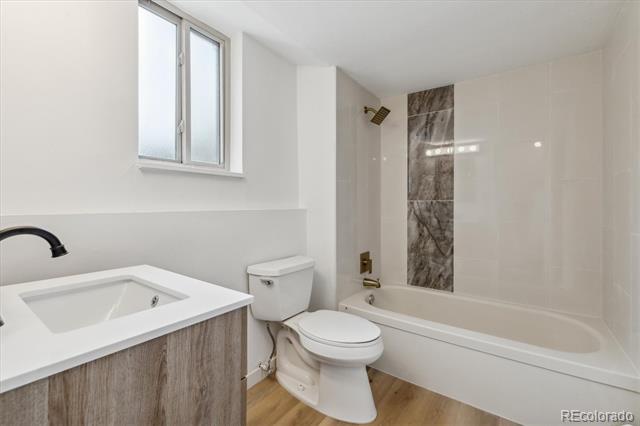 Bathroom with a white bathtub, tiled shower accent, wood-grain vanity, and high window.