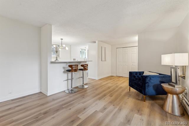 Condominium living area with a blue sofa, light wood floors, and a breakfast bar with two stools.