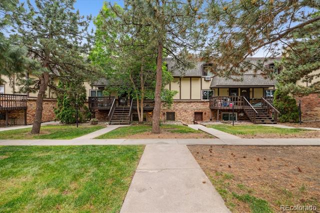 Multi-unit residential building with brick facade, raised decks, and mature trees along a walkway.
