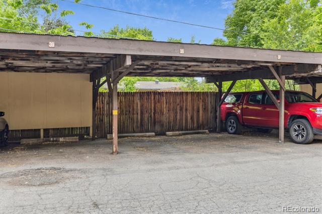Covered parking bays beside a wooden fence, with a red SUV parked in one bay.