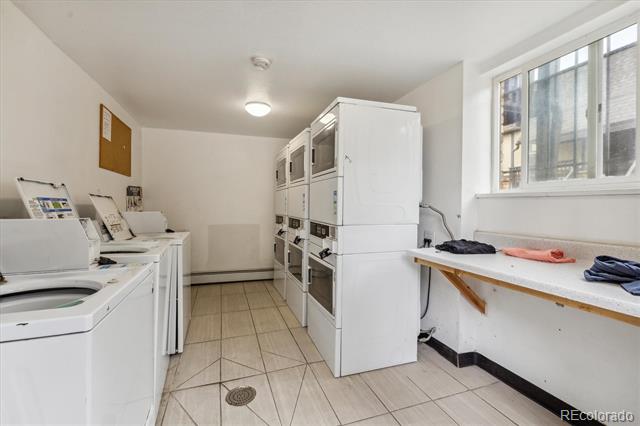 Shared laundry room with rows of white washers and dryers and a folding counter beneath a window.