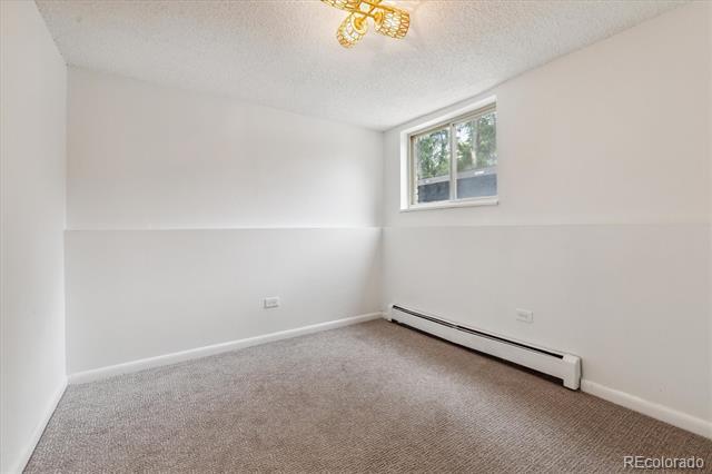 Empty bedroom with beige carpet, a high-set window, and a baseboard heater.