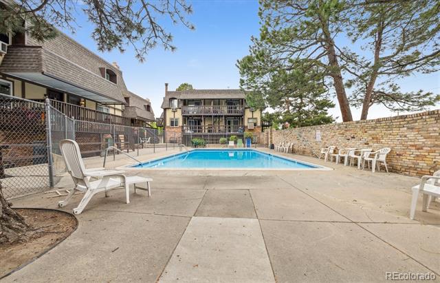 Outdoor community swimming pool with a concrete deck, lounge chairs, and surrounding residential buildings.