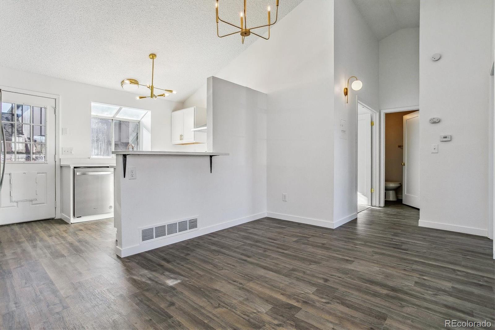 Vacant open-plan living area with a kitchen pass-through counter and gray wood-look flooring.