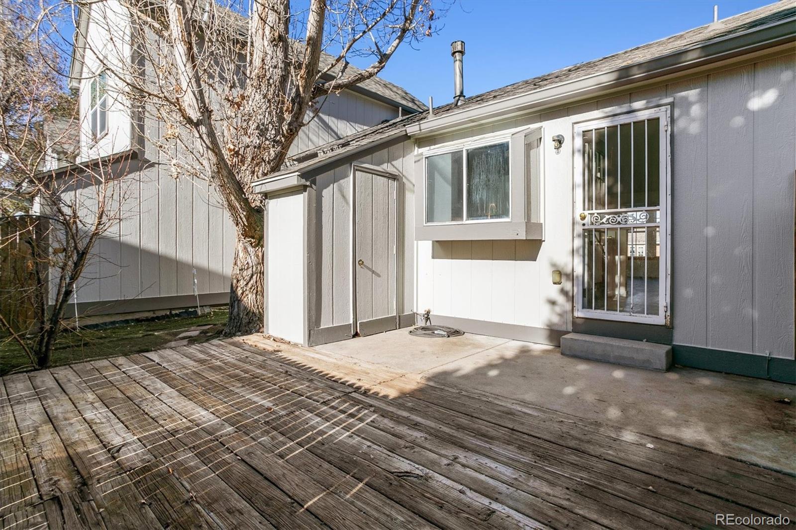 Gray townhouse patio with a barred door, concrete landing, and weathered wooden deck.