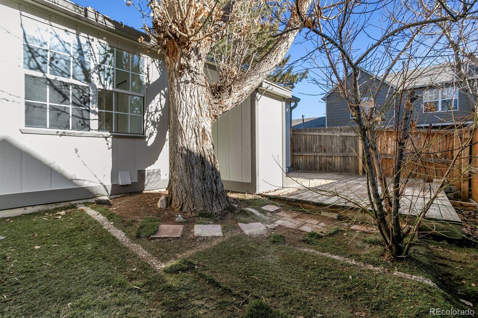 Fenced backyard with a large tree and wooden deck beside the home.