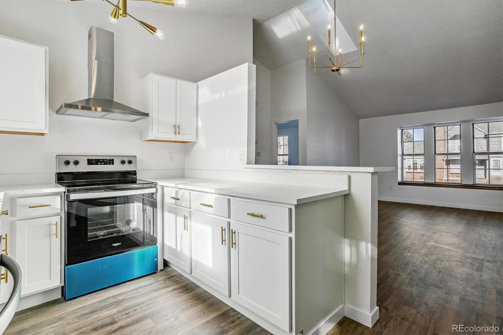 Vacant kitchen with white cabinets, brass hardware, and a peninsula opening to a sunlit living area.