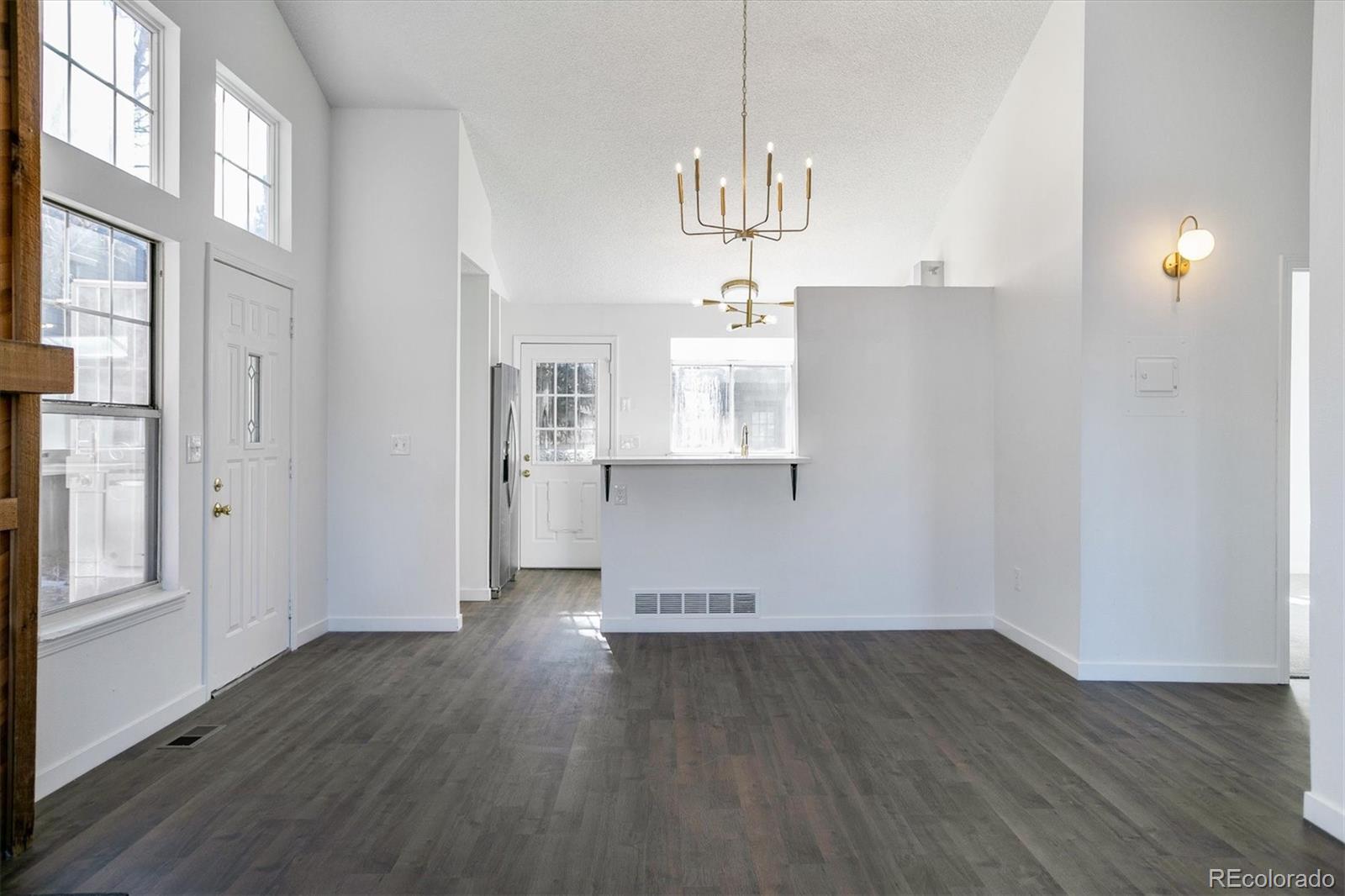 Empty open-plan living area with dark flooring, tall windows, and a kitchen pass-through.