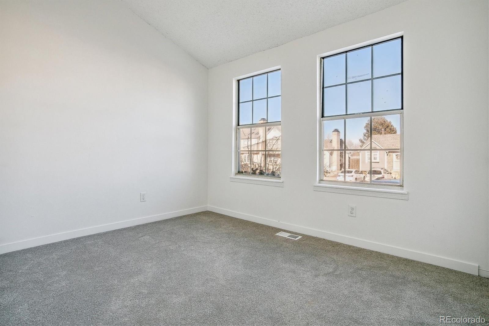 Vacant carpeted room with two large windows overlooking neighboring homes.
