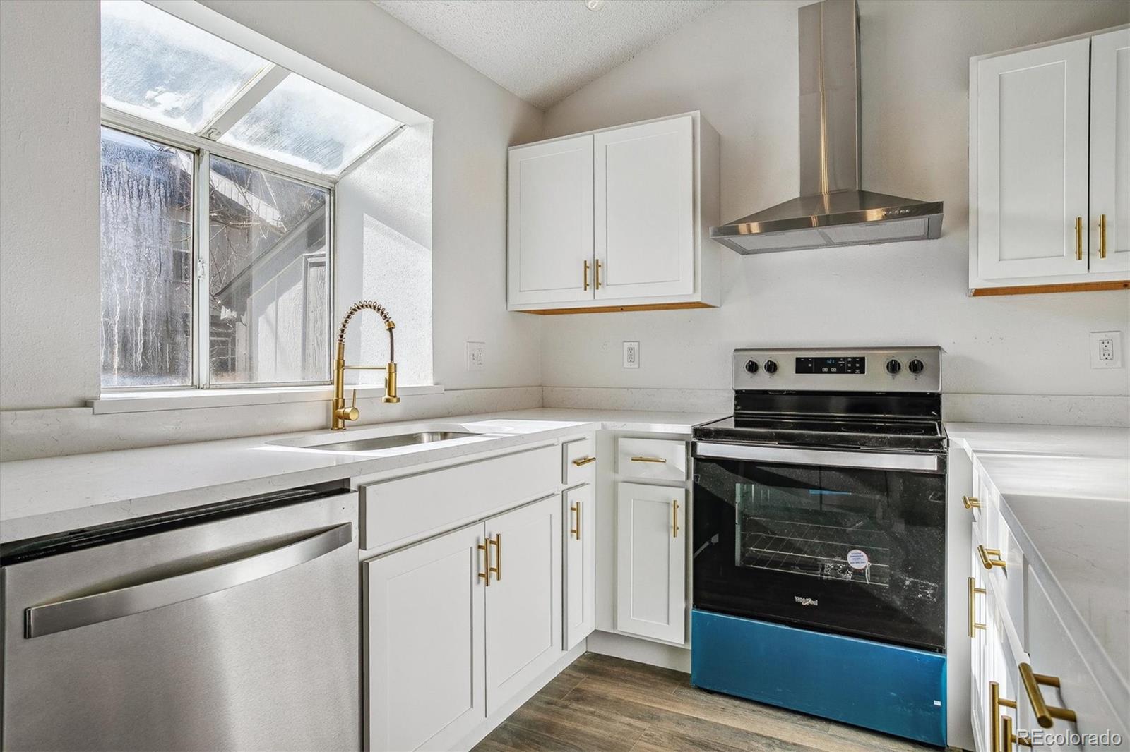 Kitchen with white cabinetry, stainless appliances, and a sunlit window with skylights.