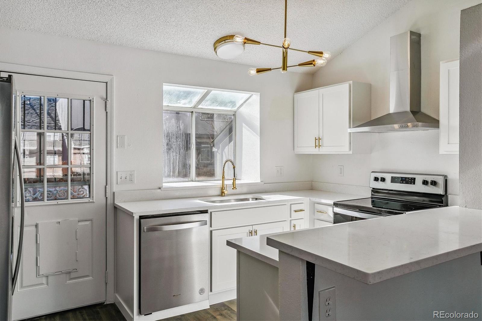 Bright white kitchen with stainless steel appliances, a breakfast peninsula, and a gold-tone ceiling light.