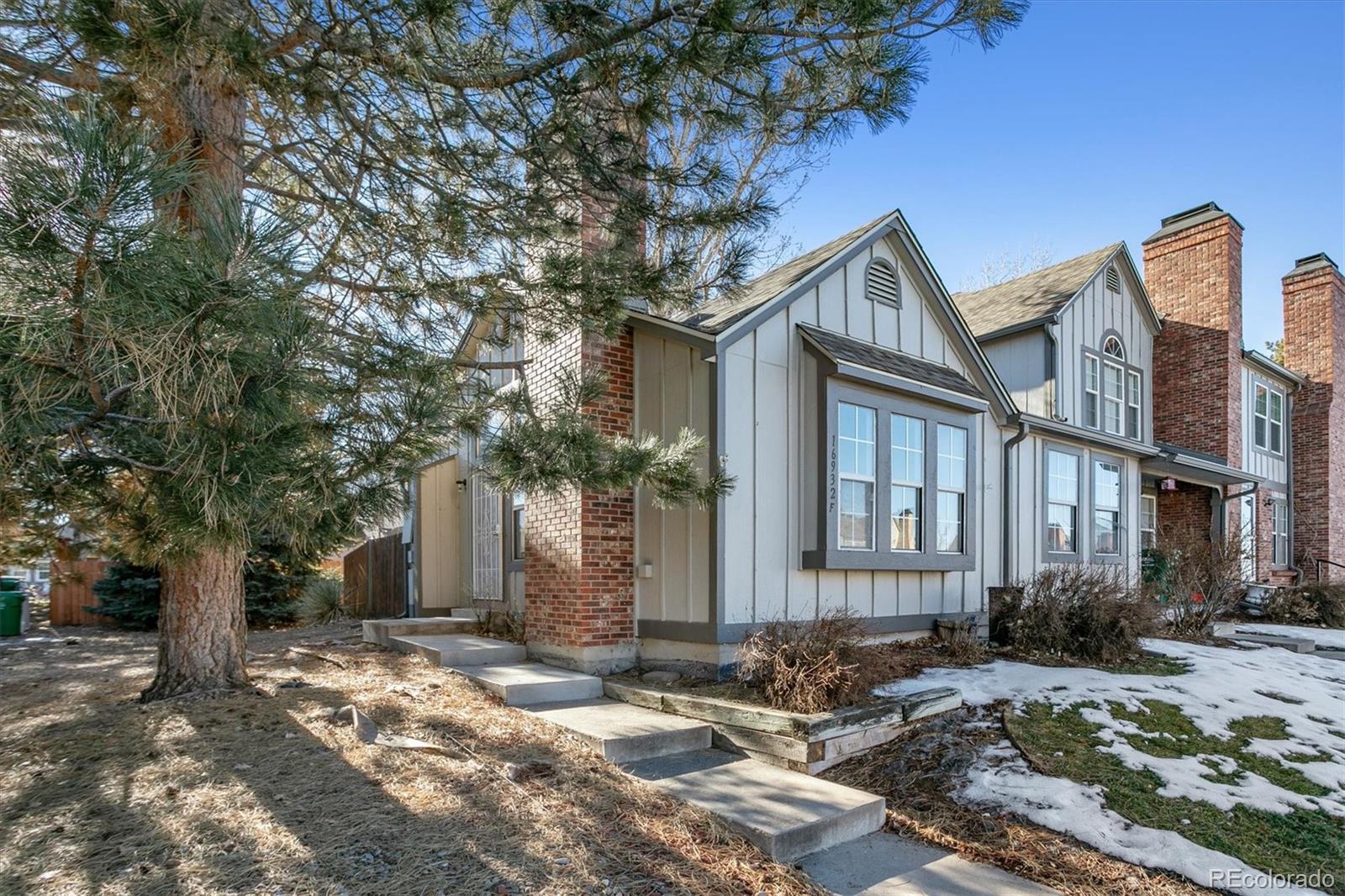 Townhouse exterior with brick accents, front steps, and a large pine tree beside the entry.