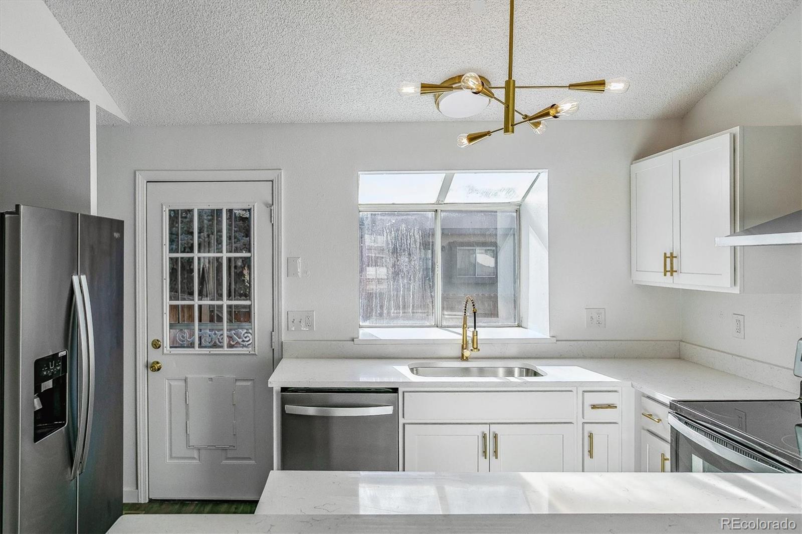 Bright white kitchen with stainless appliances, gold fixtures, and a window over the sink.