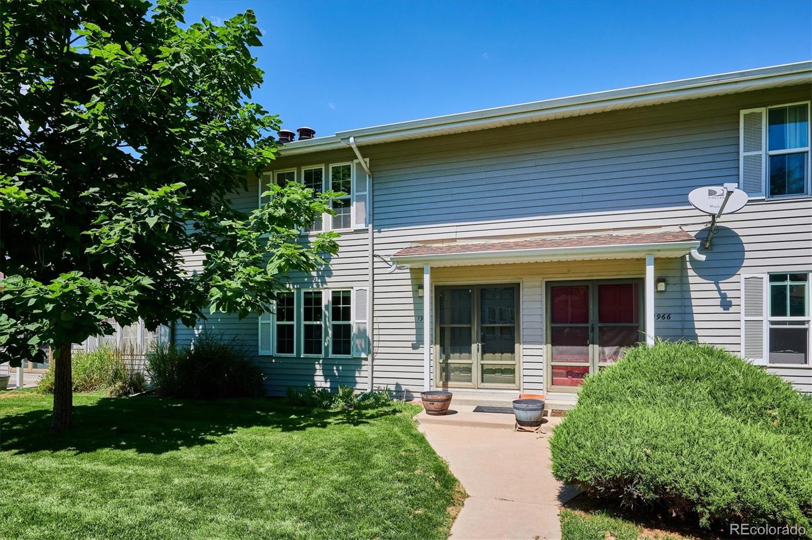 Gray two-story townhouse with white shutters, covered entrances, and a leafy tree beside the walkway.