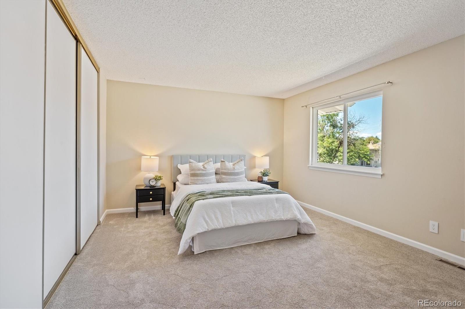 Furnished bedroom with mirrored closet doors, beige carpeting, and a large window.