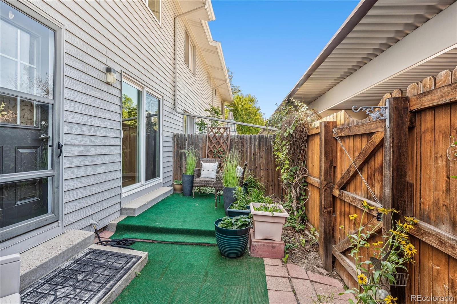 Fenced backyard patio with artificial turf, potted plants, and a small seating area.