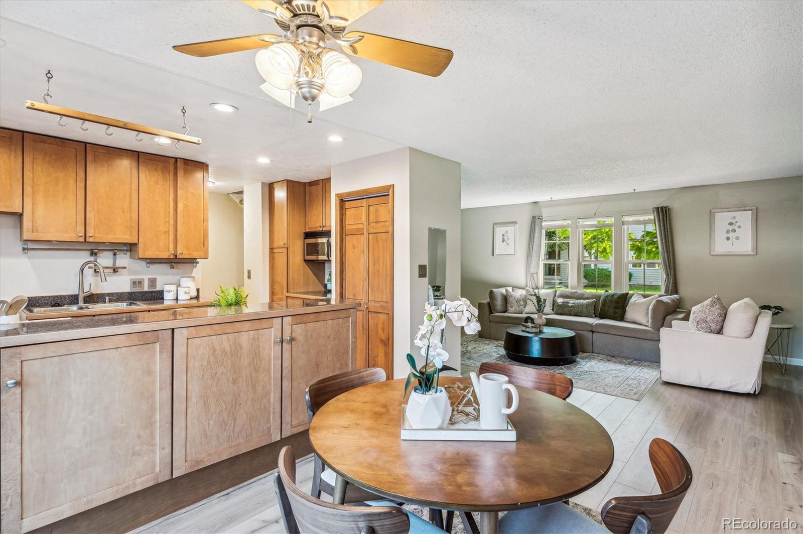 Open kitchen and dining area beside a living room with a large sectional and garden-facing windows.