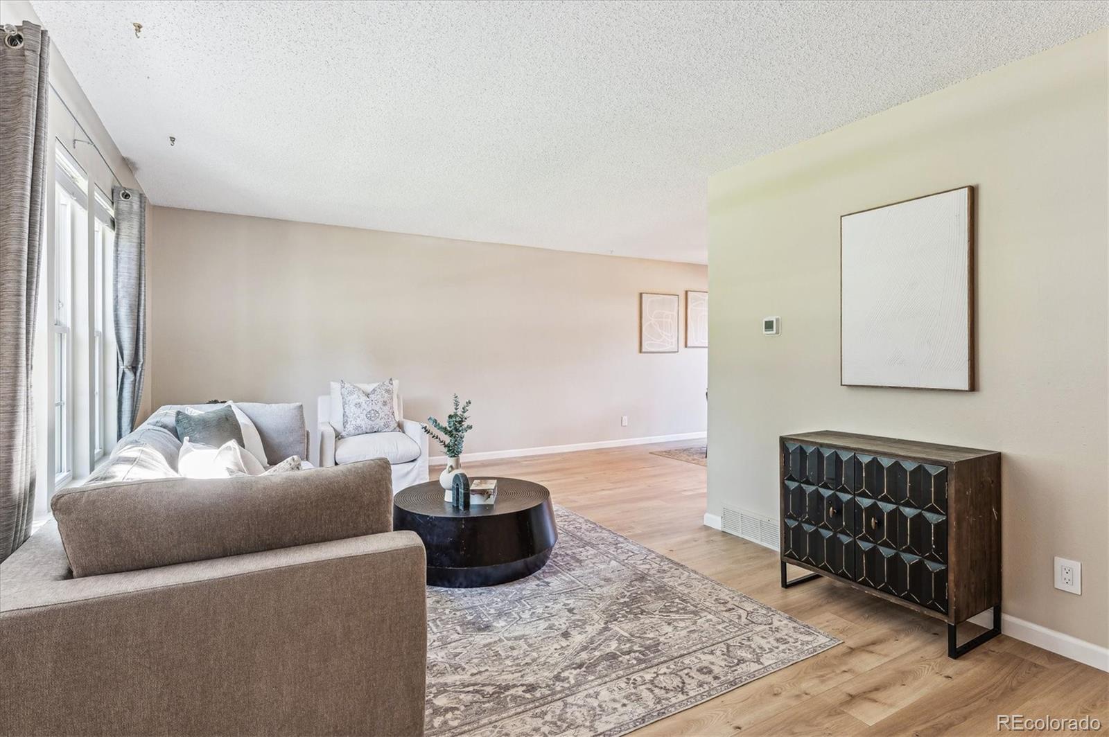 Staged living room with large curtained windows, neutral sofas, and a patterned rug.