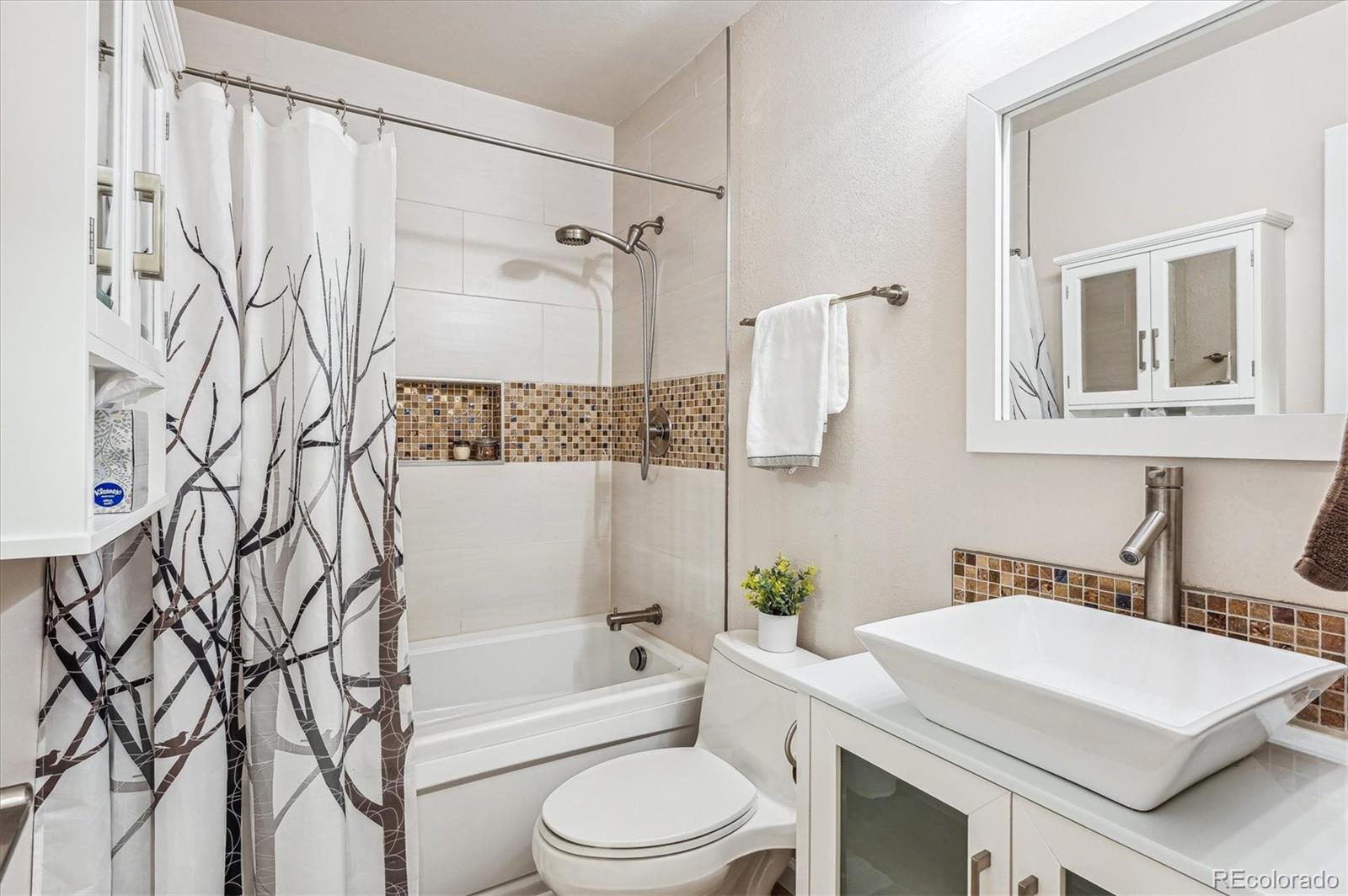 Bathroom with a patterned shower curtain, mosaic tile accents, and a white vessel sink.