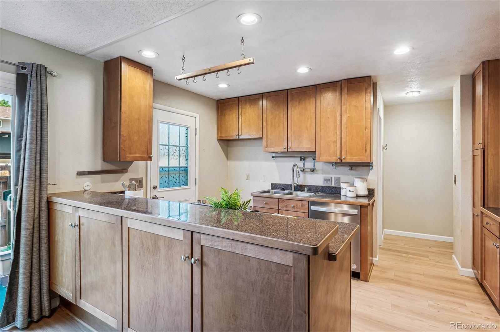 Kitchen with warm wood cabinets, a dark stone peninsula, and a stainless steel sink and dishwasher.