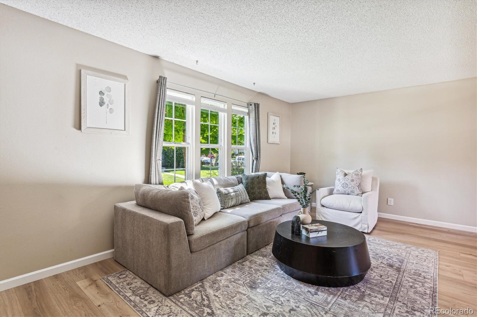 Living room with a gray sectional, white armchair, black coffee table, and three bright windows.