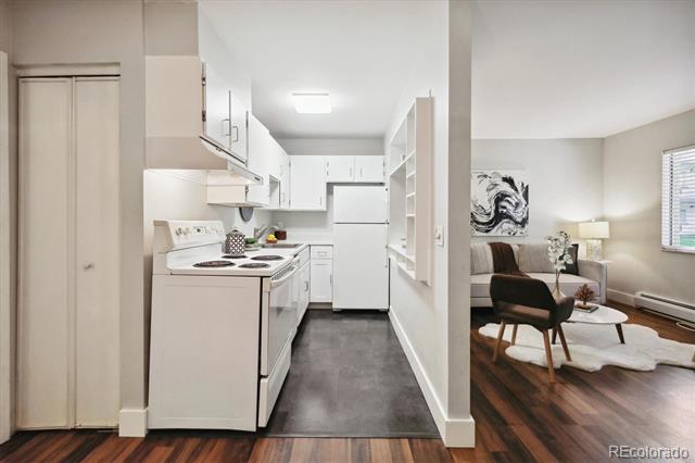 Condo kitchen and living room with white cabinetry, gray kitchen flooring, and hardwood floors.