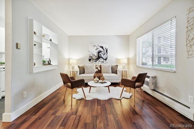 Staged living room with dark wood floors, a light sofa, brown armchairs, and a large window.