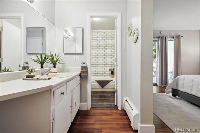 Bathroom vanity with a large mirror, doorway to a tiled tub, and bedroom visible beside it.