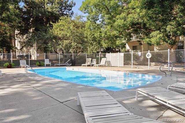 Outdoor swimming pool with lounge chairs on a paved deck beneath mature trees.