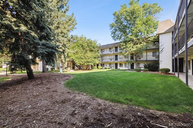 Condominium courtyard with a green lawn, mature trees, and a mulched garden bed.