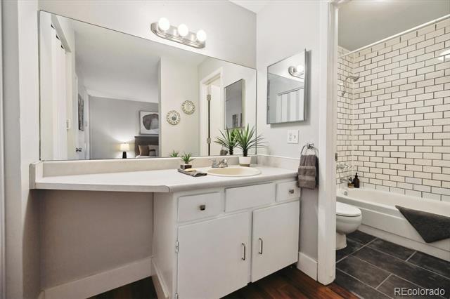 Bathroom vanity with a large mirror, white cabinetry, and an adjoining subway-tile tub.