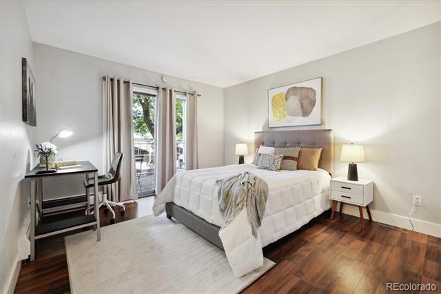 Bedroom with a gray upholstered bed, white bedding, and a desk beside tall glass doors.