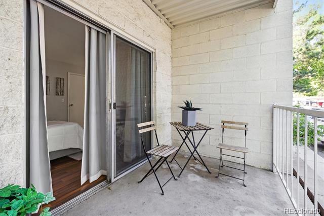 Covered apartment balcony with sliding doors, folding table, two chairs, and a potted plant.