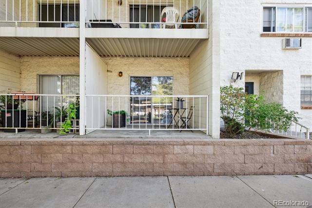 Condominium exterior with ground-floor patios, white railings, and a raised stone retaining wall.