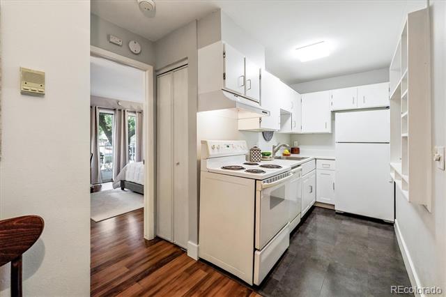 Compact kitchen with white cabinets, a white stove and refrigerator, and a doorway to a bedroom.